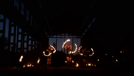 Four-women-in-leather-clothes-with-fire-dance-and-show-fire-show-a-man-with-a-flamethrower-in-the-back-plays-with-the-flame-in-slow-motion